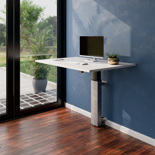 Angled view of the ConSet 501-19 modular wall mounted desk with monitor and plant beside a window