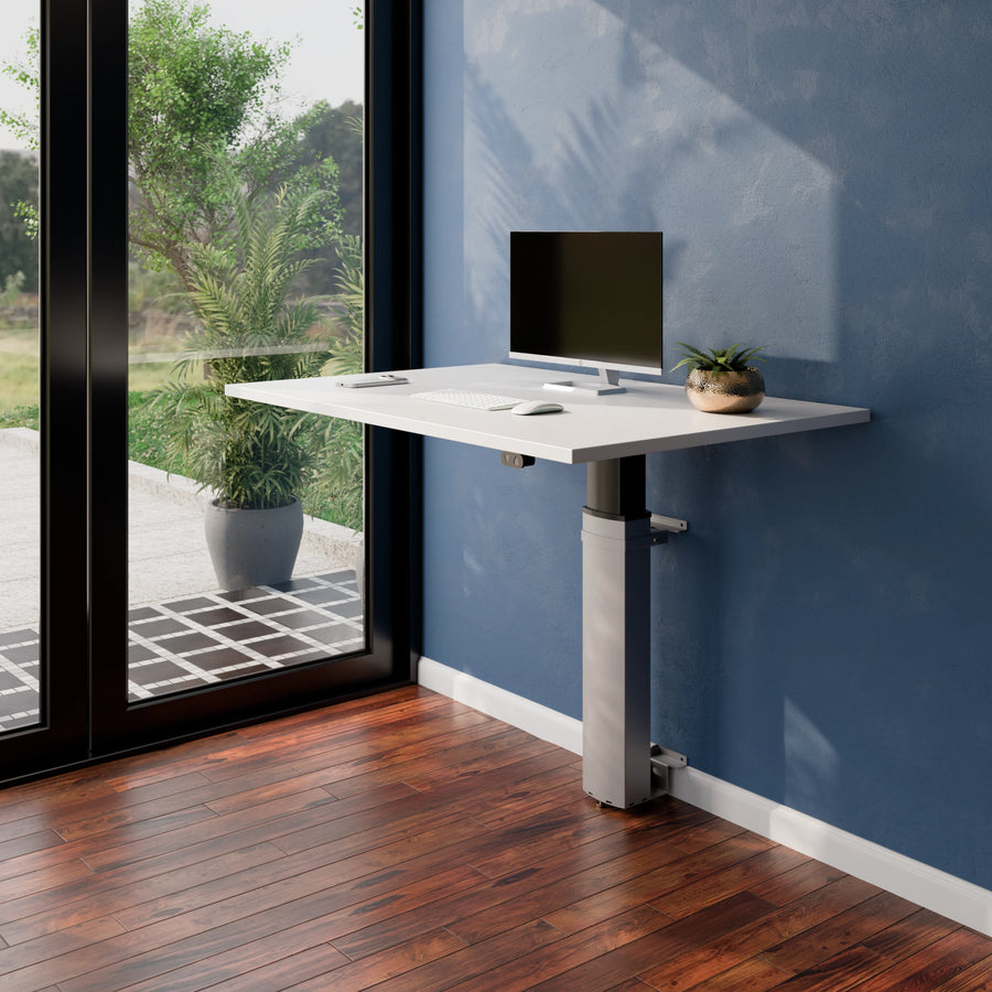 Angled view of the ConSet 501-19 modular wall mounted desk with monitor and plant beside a window