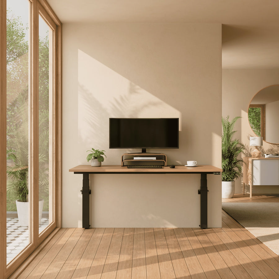 A minimalist home office featuring a wall-mounted electric standing desk with an oak wood top and black legs against a beige wall.